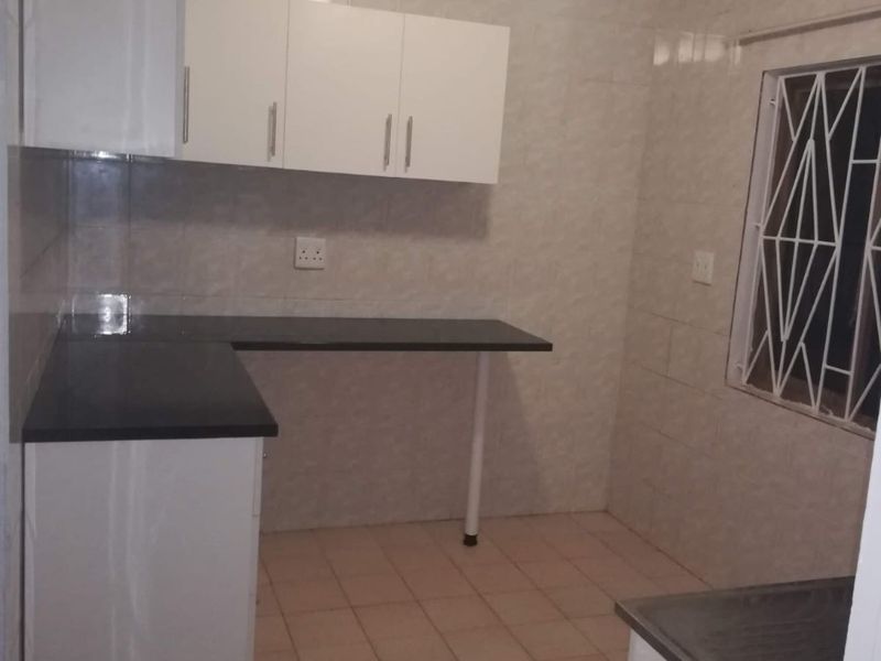 A functional kitchen featuring white built-in cabinetry, dark laminate countertops, fully tiled walls, and tiled flooring with a secure window.