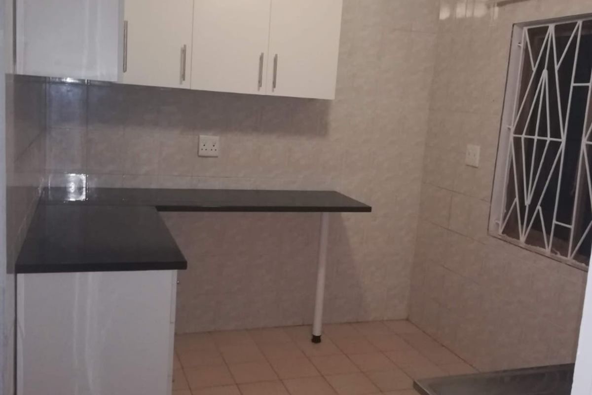A functional kitchen featuring white built-in cabinetry, dark laminate countertops, fully tiled walls, and tiled flooring with a secure window.