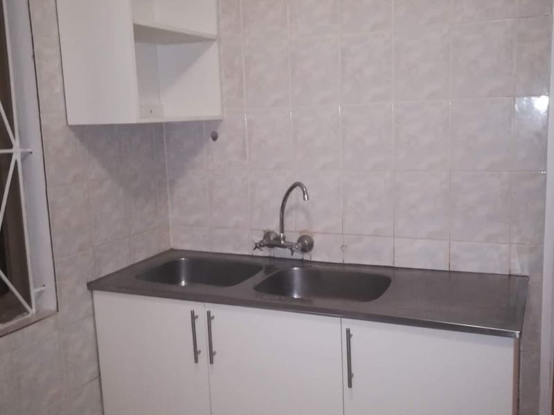 A functional kitchen area featuring a stainless steel double sink, white cabinetry, wall-mounted shelving, and tiled finishes throughout.