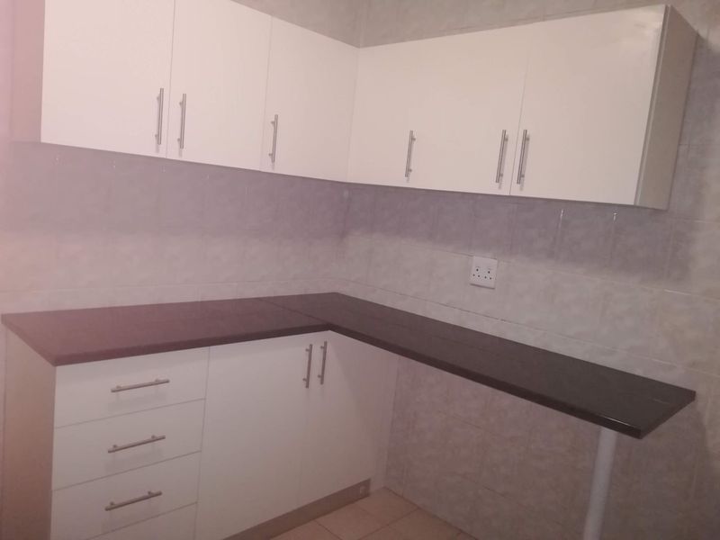 A clean, functional kitchen area featuring white built-in cabinetry, dark laminate countertops, and a tiled backsplash.