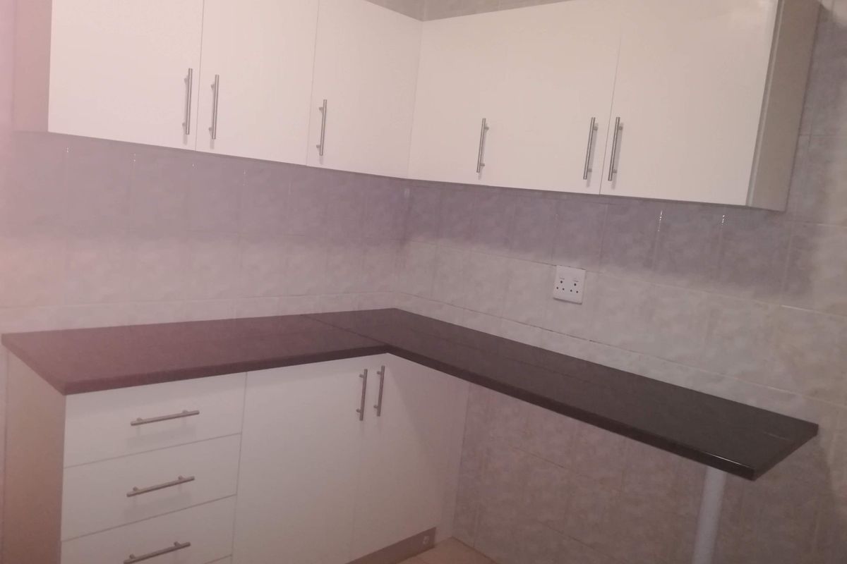 A clean, functional kitchen area featuring white built-in cabinetry, dark laminate countertops, and a tiled backsplash.