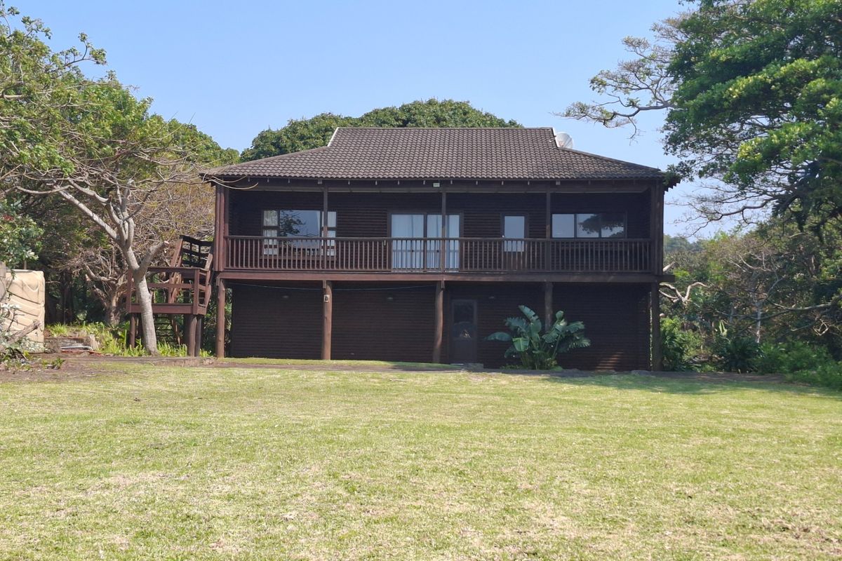 A two-story timber-clad house featuring a raised wooden deck, balcony, and external staircase, set within a spacious garden area.