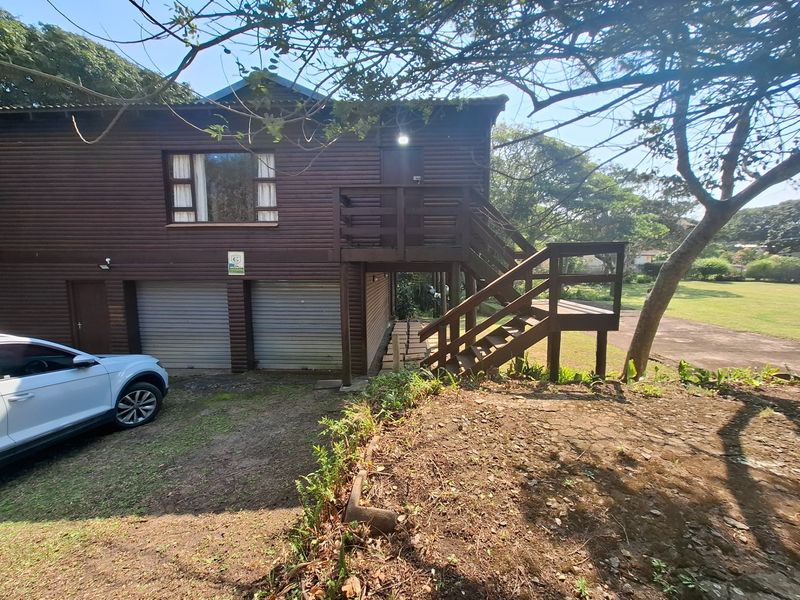 A two-story timber-clad house featuring a double garage with roller doors and an external staircase leading to an elevated balcony.