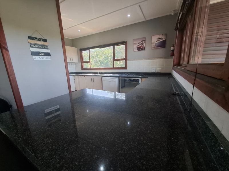 A functional kitchen featuring dark granite countertops, a built-in oven, gas hob, and tiled backsplash with ample natural light from timber-framed windows.
