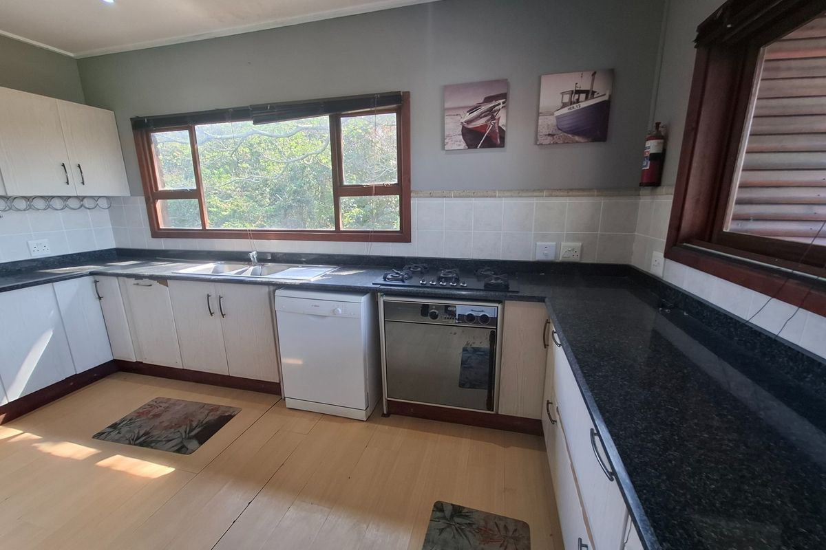 A functional kitchen featuring granite countertops, built-in cabinetry, a gas hob, and an integrated oven, with large windows providing natural light.