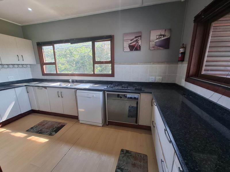 A functional kitchen featuring granite countertops, built-in cabinetry, a gas hob, and an integrated oven, with large windows providing natural light.