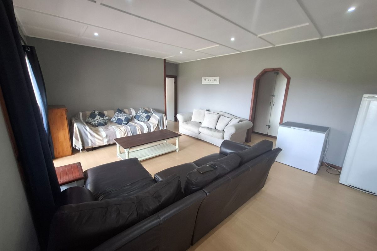 A spacious living room featuring laminate flooring, a panelled ceiling with recessed downlights, and neutral wall tones.