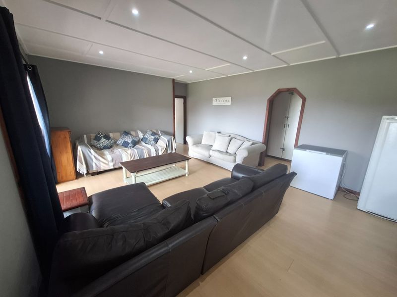 A spacious living room featuring laminate flooring, a panelled ceiling with recessed downlights, and neutral wall tones.
