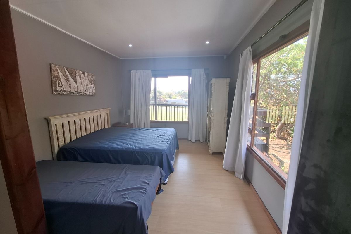 Spacious bedroom featuring timber-look flooring, recessed downlights, and large windows providing natural light and garden views.