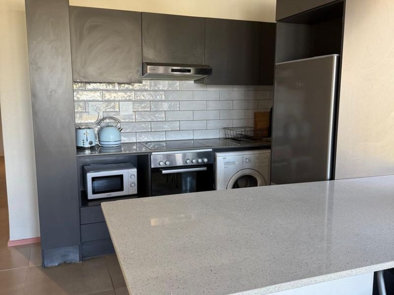 Modern kitchen featuring grey cabinetry, stone countertops, subway tile backsplash, and a functional breakfast bar with integrated appliance spaces.