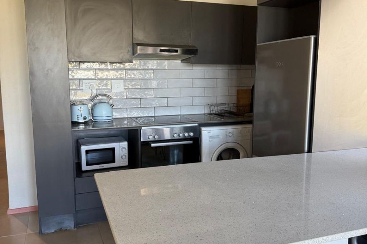 Modern kitchen featuring grey cabinetry, stone countertops, subway tile backsplash, and a functional breakfast bar with integrated appliance spaces.