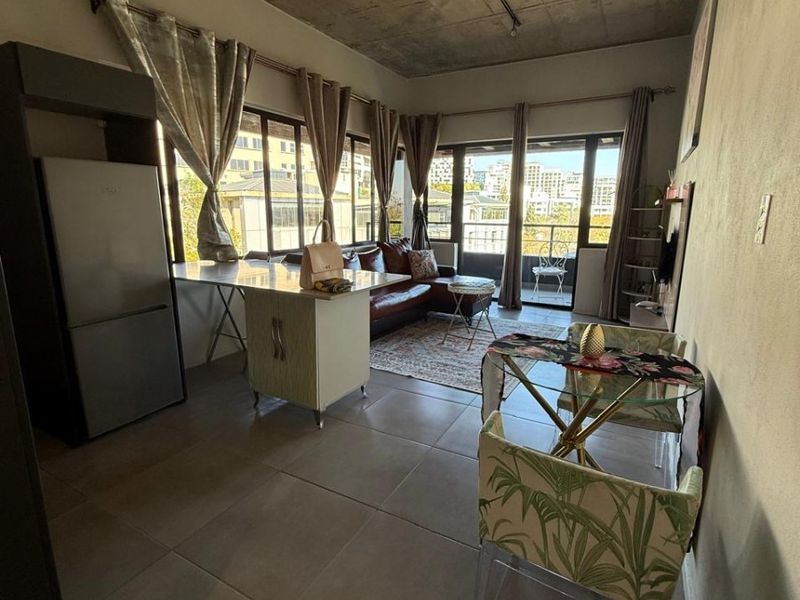 Open-plan living area featuring an exposed concrete ceiling, large format floor tiles, and direct access to a private balcony through sliding glass doors.