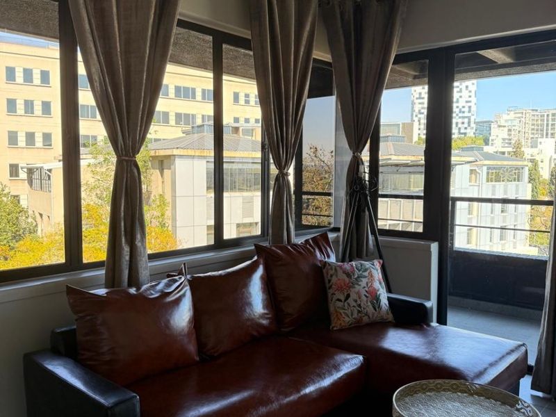A bright living room featuring large windows, a sliding glass door leading to a balcony, and an industrial-style exposed concrete ceiling.