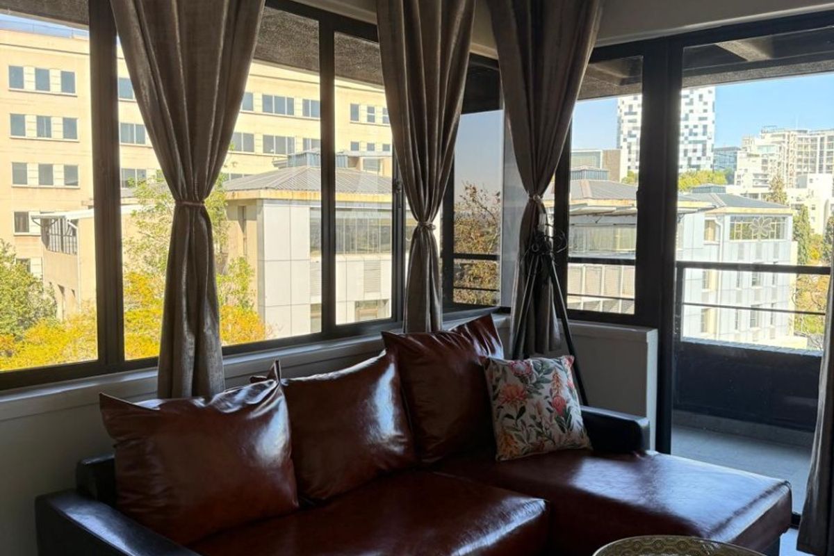 A bright living room featuring large windows, a sliding glass door leading to a balcony, and an industrial-style exposed concrete ceiling.