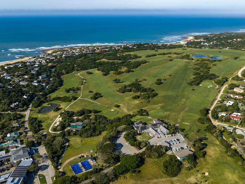Aerial view of a coastal residential estate featuring a golf course, clubhouse, tennis courts, and surrounding natural landscape.