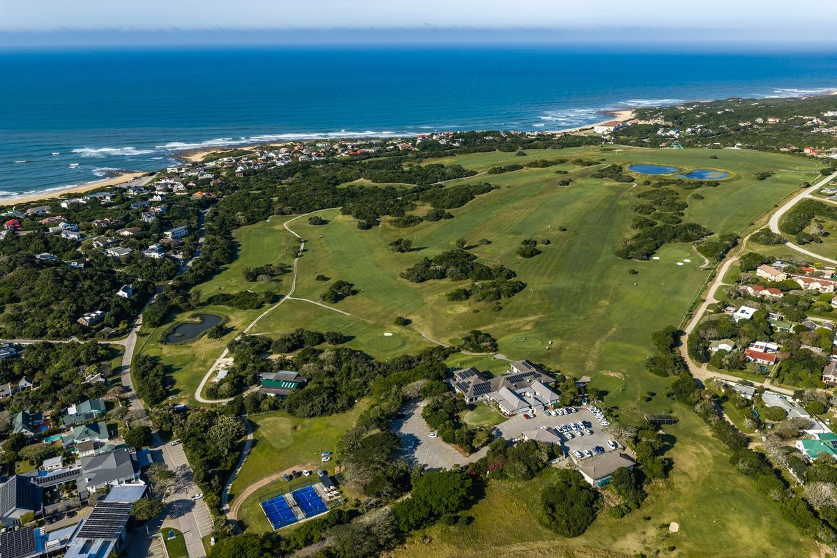 Aerial view of a coastal residential estate featuring a golf course, clubhouse, tennis courts, and surrounding natural landscape.