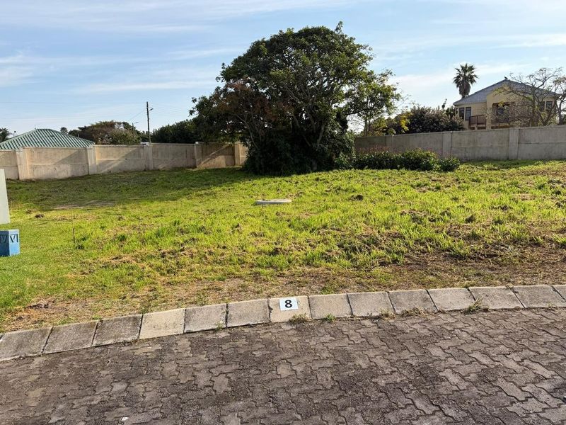 A vacant residential plot featuring a level grassed area, enclosed by a precast concrete boundary wall, with direct street access.