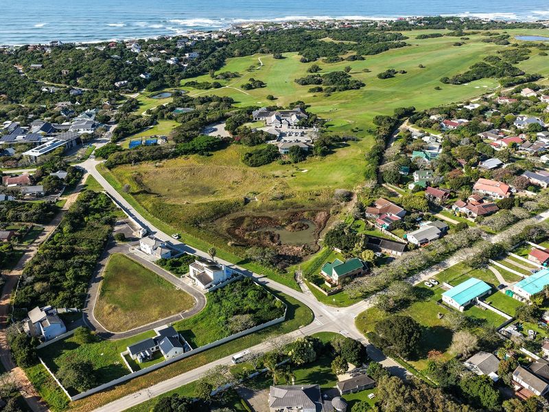 Aerial view of a vacant residential plot situated in a coastal estate, featuring proximity to a golf course and established neighborhood infrastructure.