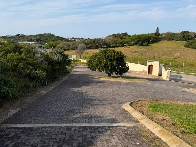 A view of a paved driveway leading into a residential estate, featuring a security gate and a small guard house structure.