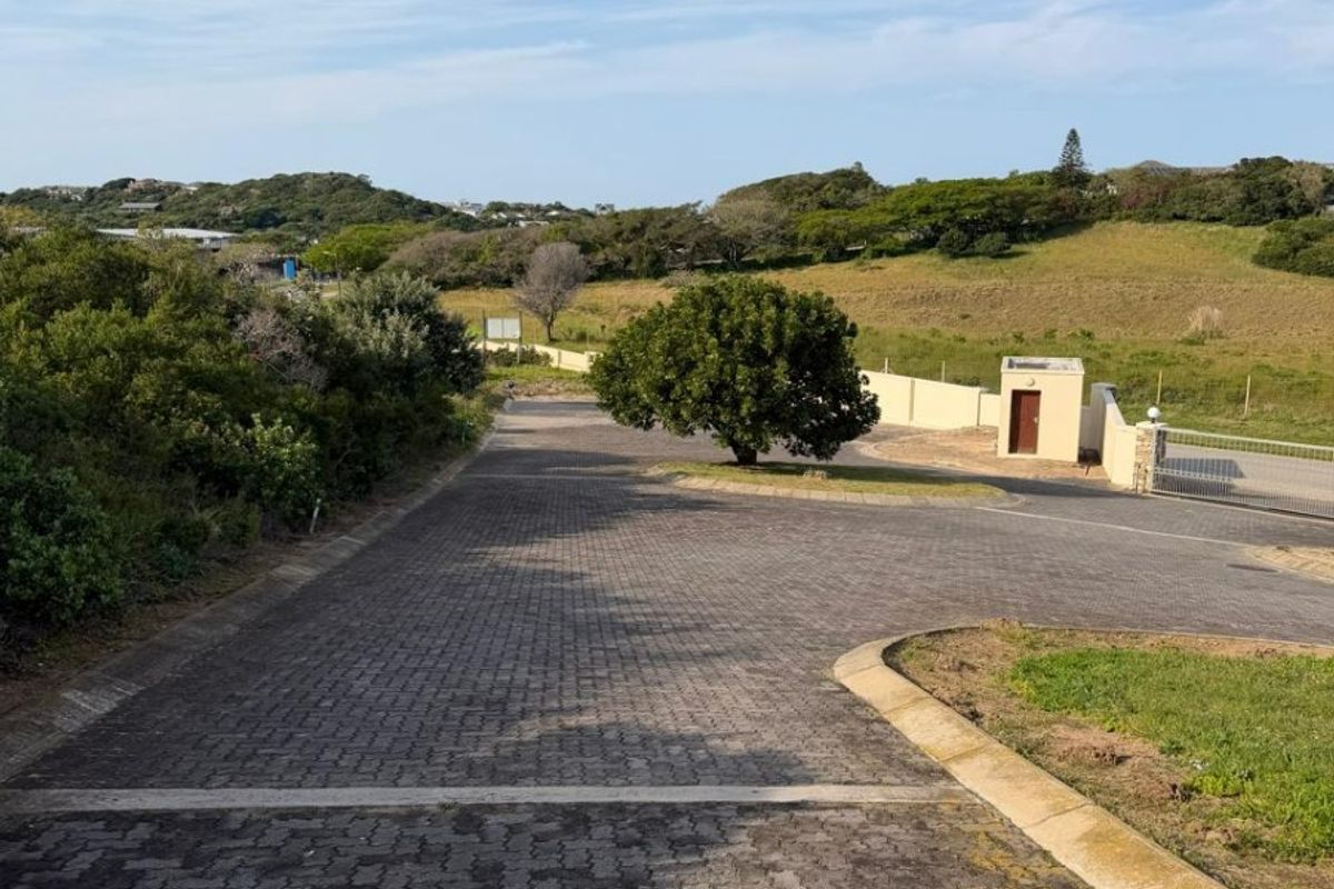 A view of a paved driveway leading into a residential estate, featuring a security gate and a small guard house structure.