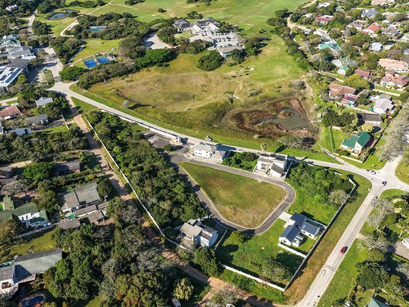 Aerial view of a residential development area featuring vacant plots, paved access roads, and established perimeter fencing within a landscaped estate setting.