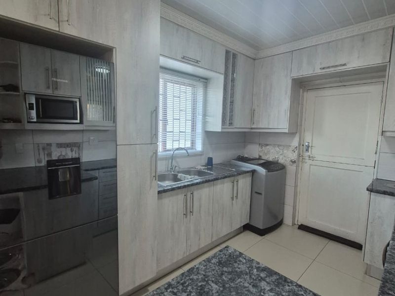 A functional kitchen featuring light-toned cabinetry, granite countertops, a double basin sink, and built-in microwave, with tiled flooring and a clean, practical layout.