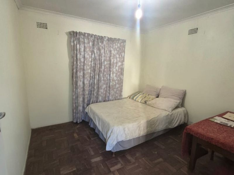 A simple bedroom featuring parquet flooring and neutral walls, providing a functional space with basic finishes.