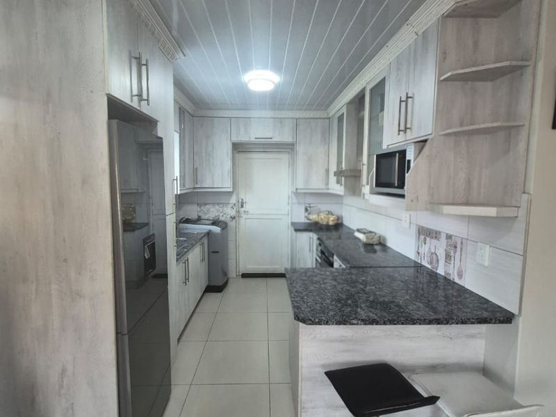 A functional kitchen featuring light wood-grain cabinetry, granite countertops, built-in microwave, and tiled flooring with a clean, modern layout.