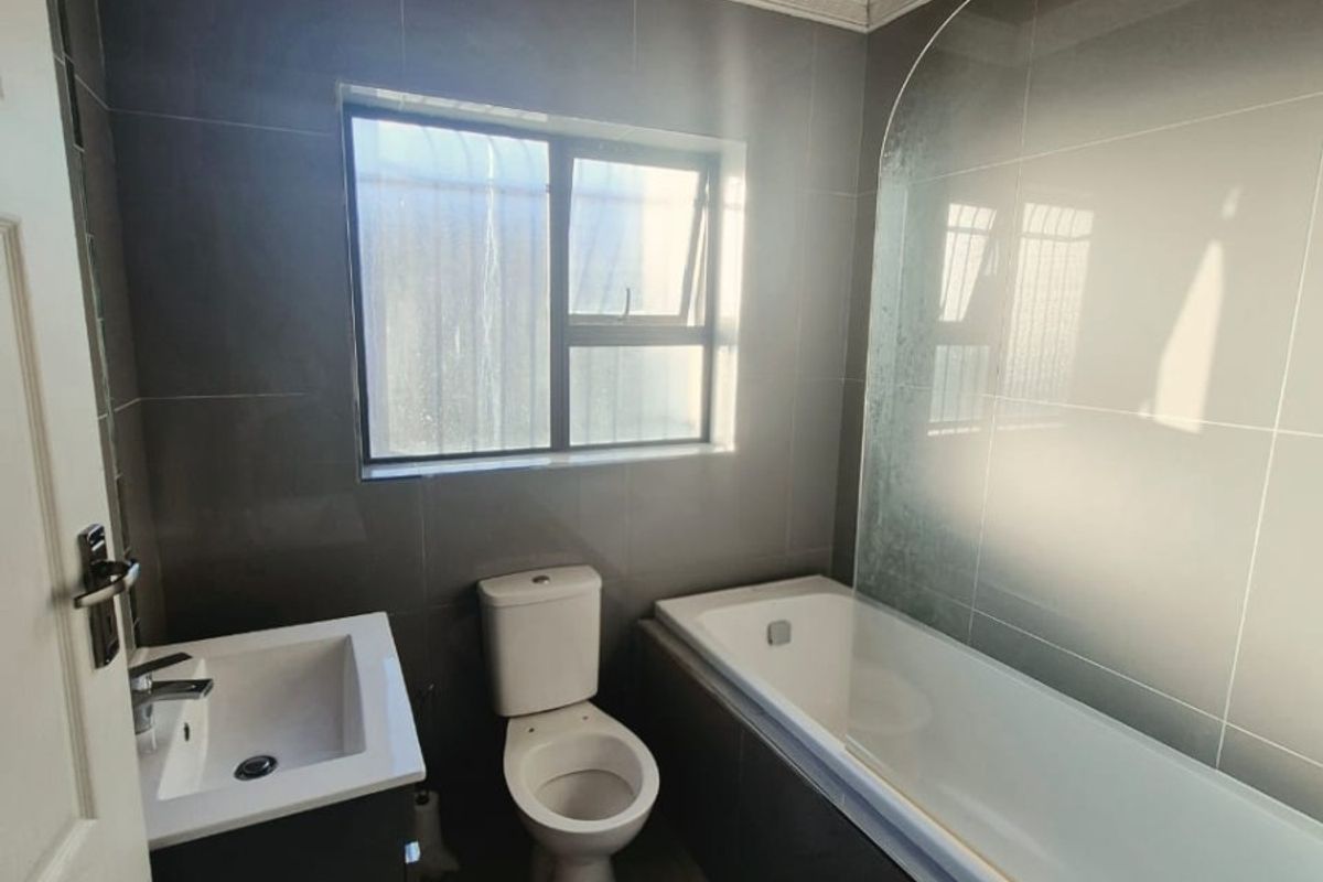A modern bathroom featuring a bathtub with a glass screen, a vanity basin, a toilet, and a distinctive timber ceiling with tiled finishes.