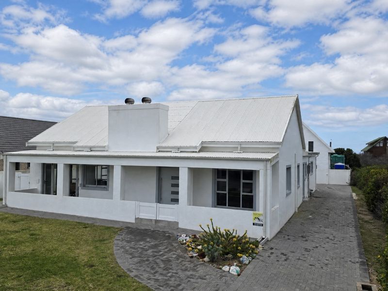 A well-maintained single-story house featuring a white exterior, corrugated metal roof, covered patio, and paved driveway.