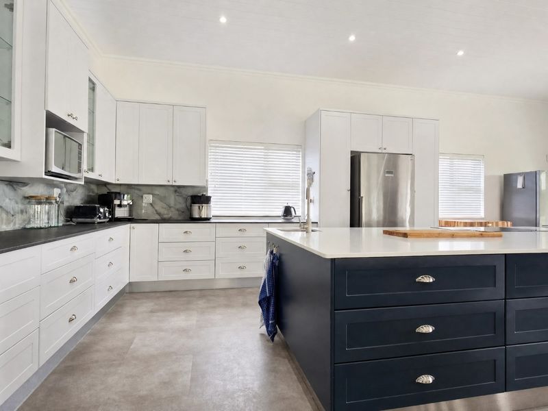 Modern kitchen featuring a large central island, white cabinetry, dark contrasting base units, quartz countertops, and high-quality finishes throughout.