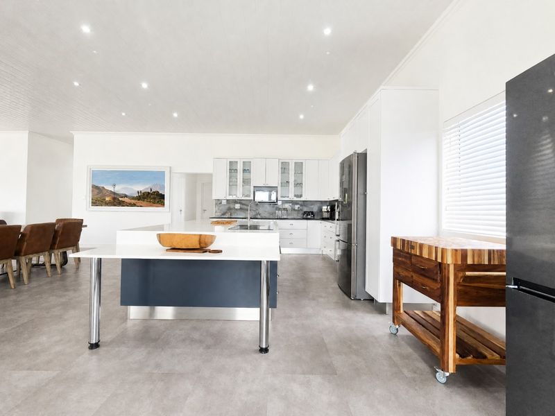 Spacious open-plan kitchen and dining area featuring modern white cabinetry, a large central island, recessed lighting, and sleek tiled flooring.