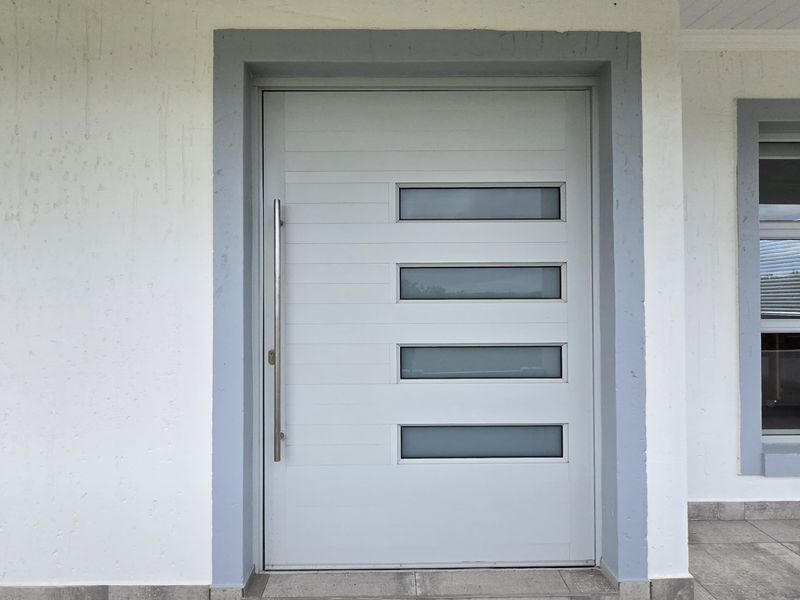 A modern front entrance featuring a contemporary door with frosted glass panels, stainless steel hardware, and a tiled porch area.