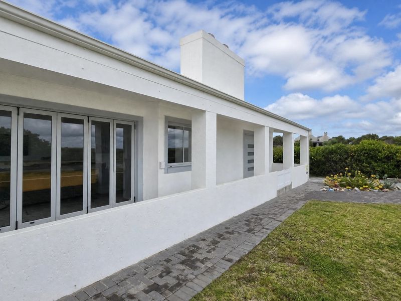 A well-maintained rear exterior view featuring a covered patio, paved walkway, and bi-fold doors leading into the home.