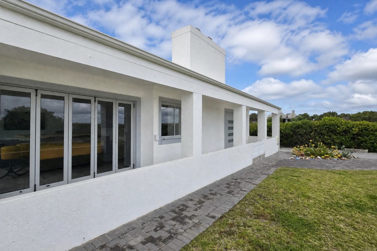 A well-maintained rear exterior view featuring a covered patio, paved walkway, and bi-fold doors leading into the home.