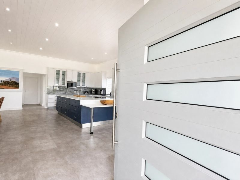 Modern open-plan living area featuring a contemporary kitchen with a large island, sleek cabinetry, and tiled flooring, viewed from the entrance.