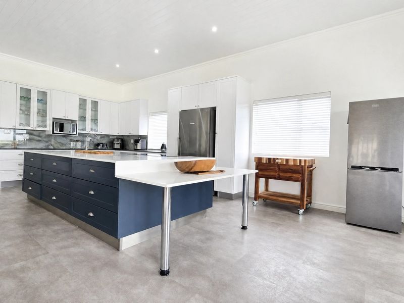 Modern kitchen featuring a large central island with dark blue cabinetry, white stone countertops, ample storage, and stainless steel appliances.