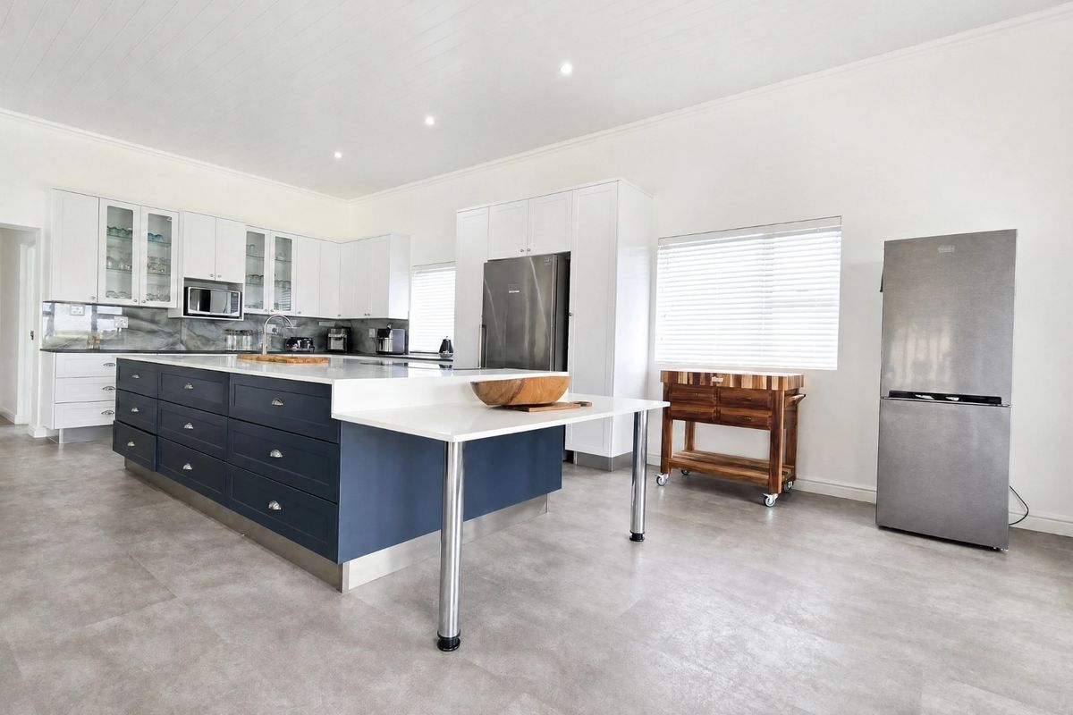 Modern kitchen featuring a large central island with dark blue cabinetry, white stone countertops, ample storage, and stainless steel appliances.