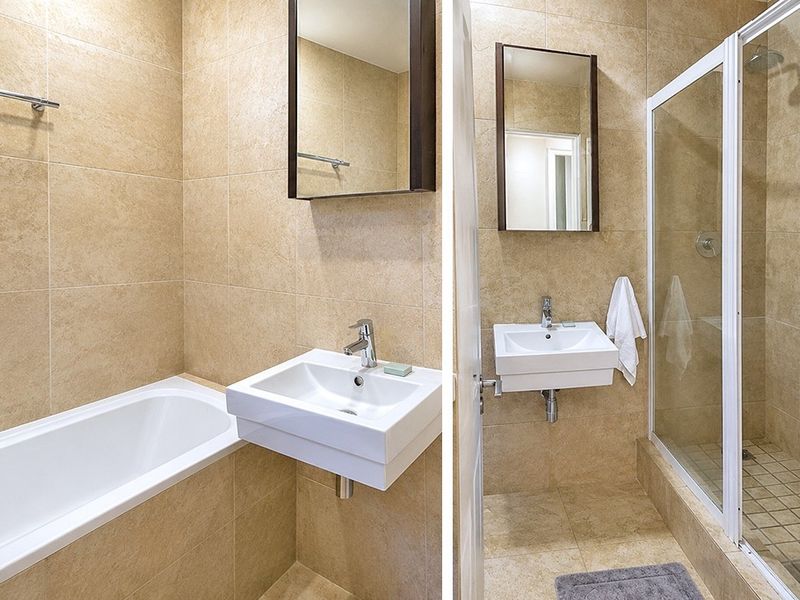 A clean, tiled bathroom featuring a wall-mounted basin, a bathtub, and a separate glass-enclosed shower area.