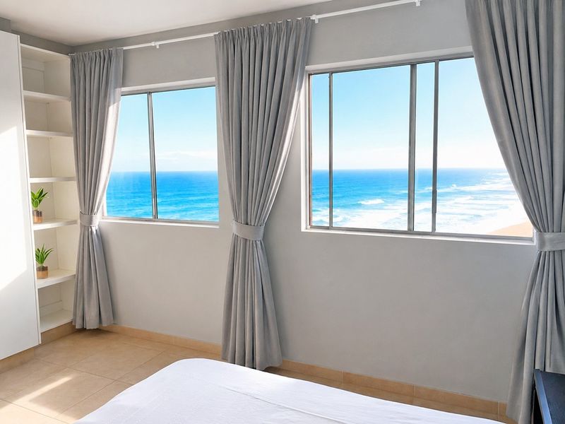 A bright bedroom featuring built-in shelving, tiled flooring, and large windows offering expansive ocean views.