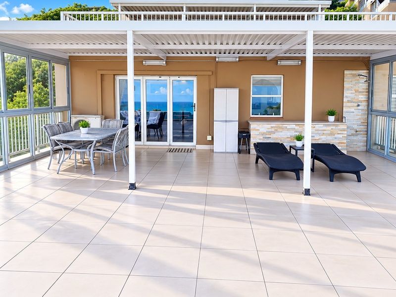 Spacious covered patio featuring tiled flooring, stone-clad accents, and large sliding glass doors, offering a seamless transition to outdoor living.