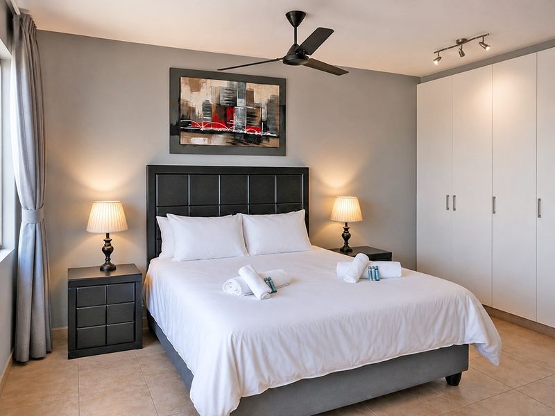 A well-maintained bedroom featuring neutral walls, tiled flooring, a modern ceiling fan, and ample built-in wardrobe storage.