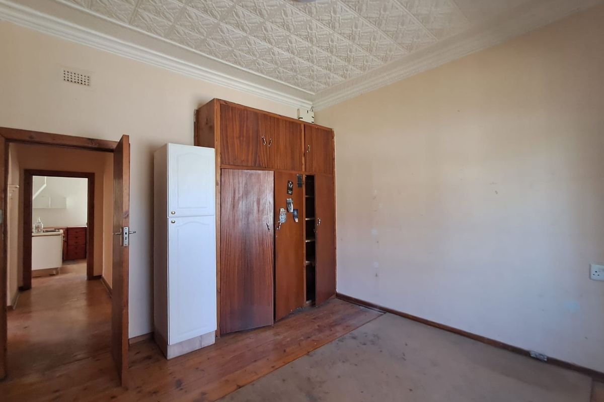 A bedroom featuring original pressed metal ceilings, wooden flooring, and built-in wooden cupboards, offering a classic foundation for renovation.