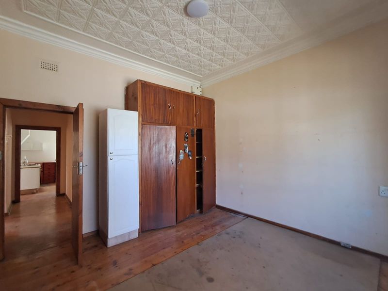 A bedroom featuring original pressed metal ceilings, wooden flooring, and built-in wooden cupboards, offering a classic foundation for renovation.