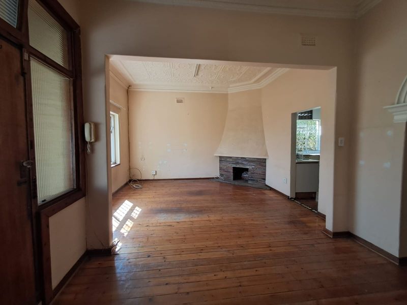 Spacious living area featuring original timber flooring, a character fireplace, and decorative ceiling details, offering a blank canvas for renovation.
