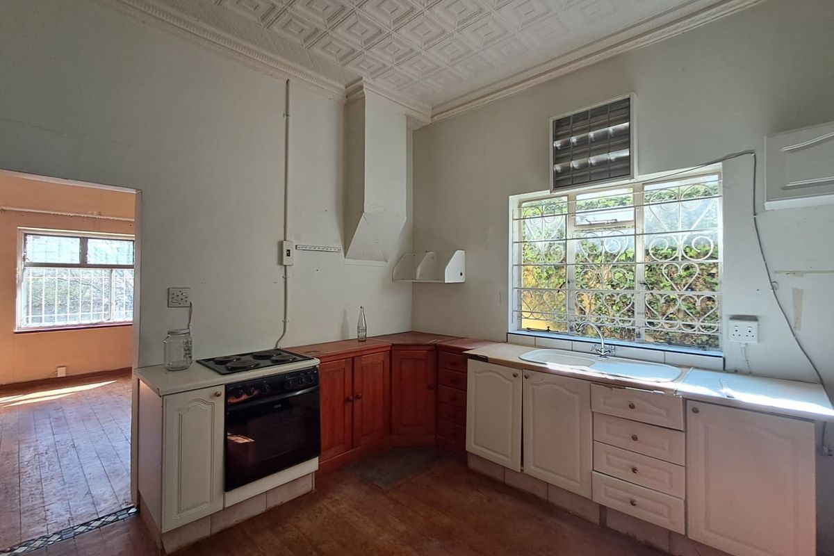 A dated kitchen featuring built-in cabinetry, an electric stove, and a double sink, with original decorative ceiling tiles and security bars on the windows.