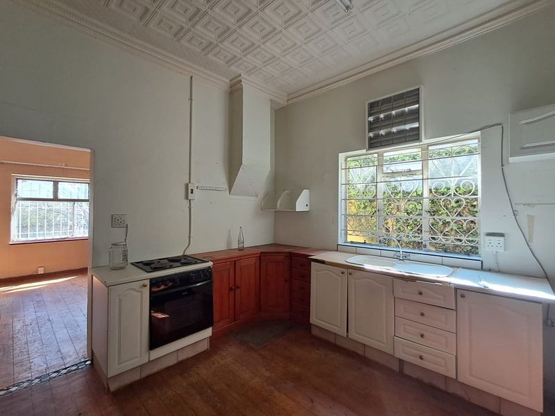 A dated kitchen featuring built-in cabinetry, an electric stove, and a double sink, with original decorative ceiling tiles and security bars on the windows.