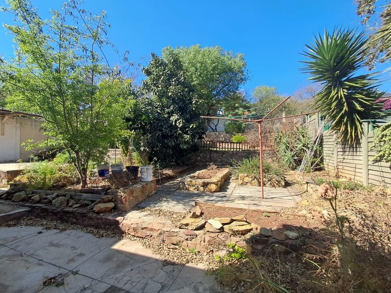 A spacious rear garden featuring stone retaining walls, paved sections, and established trees, offering potential for landscaping and outdoor living improvements.