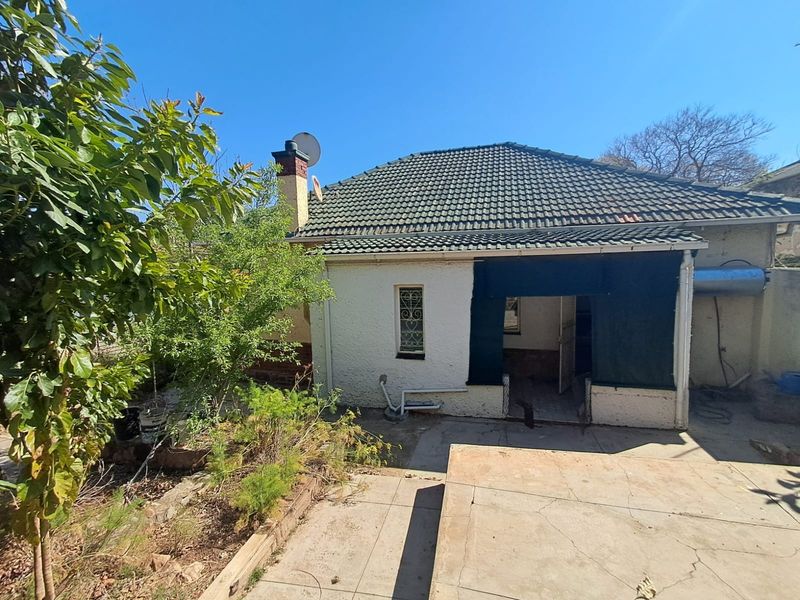 Rear view of the property featuring a tiled roof, chimney, concrete patio area, and security features including bars and a gate.