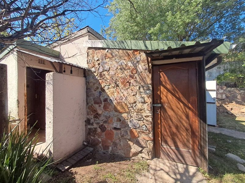 Rear exterior view of the property featuring stone cladding, a corrugated metal roof, and a timber entrance door.